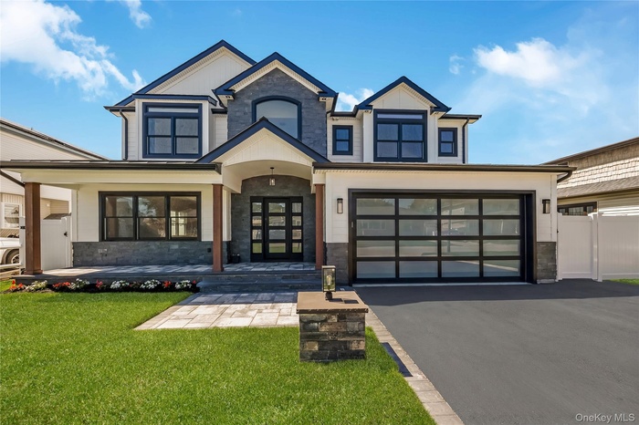Magnificent contemporary two-story home featuring a stone and siding exterior, multi-pane black garage door, paved driveway, manicured lawn, and a cov
