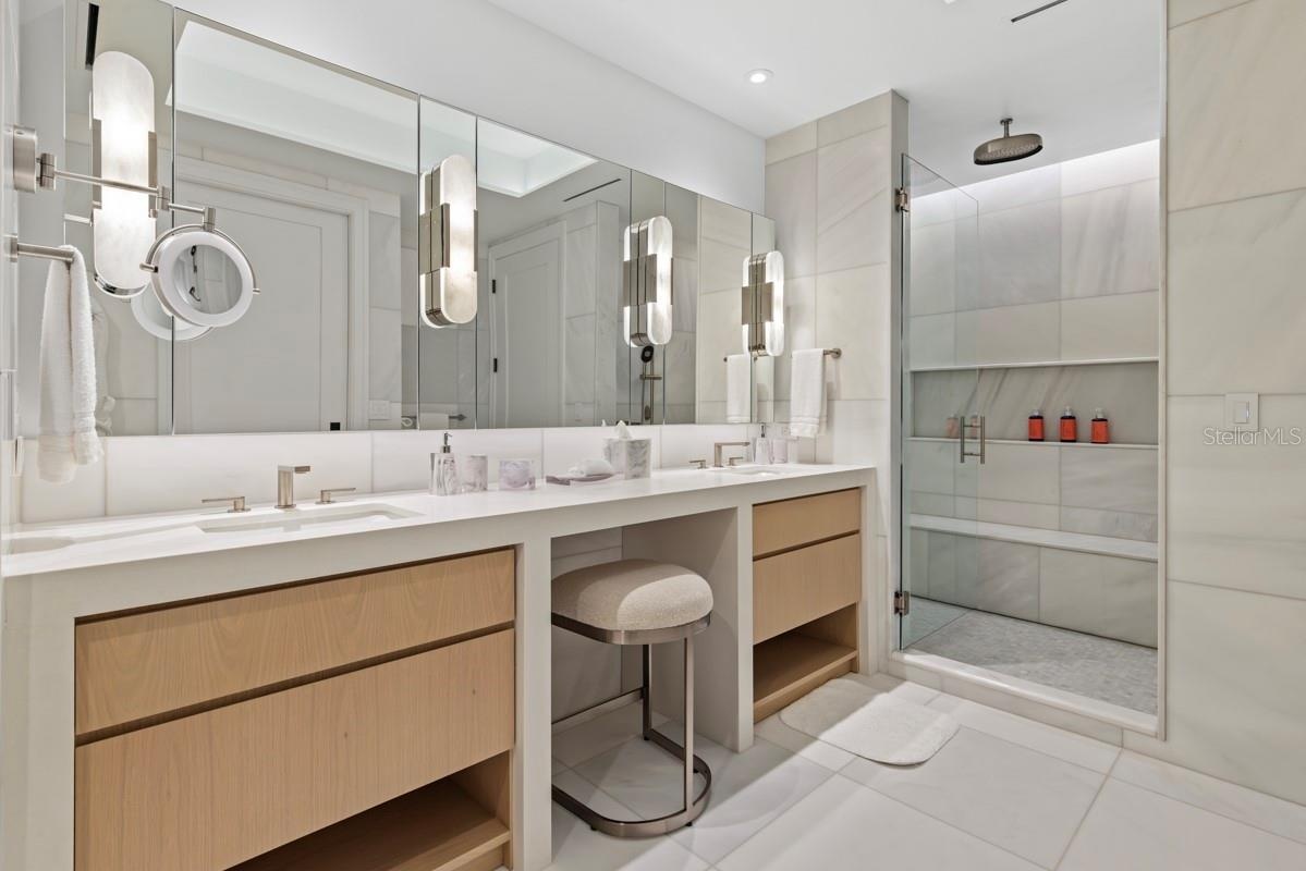 Luxurious primary bath featuring custom vanities, marble floors, walls and shower and lavish freestanding soaking tub.