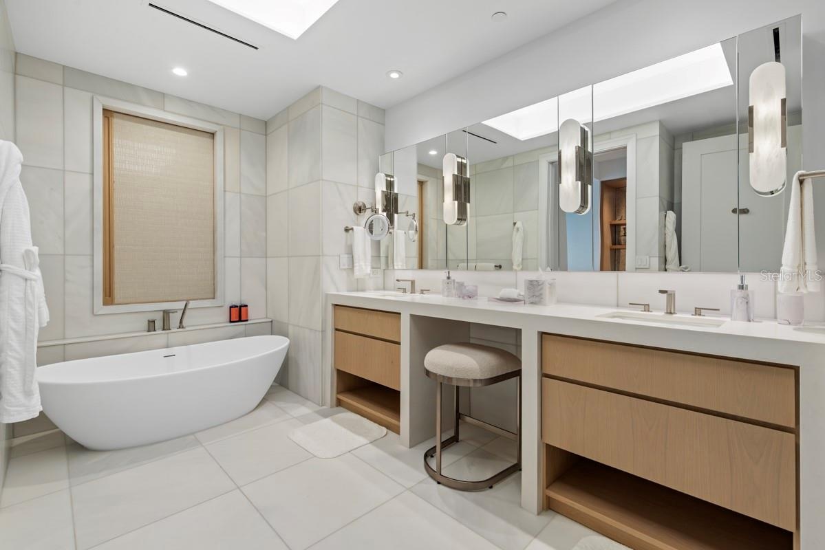 Luxurious primary bath featuring custom vanities, marble floors, walls and shower and lavish freestanding soaking tub.