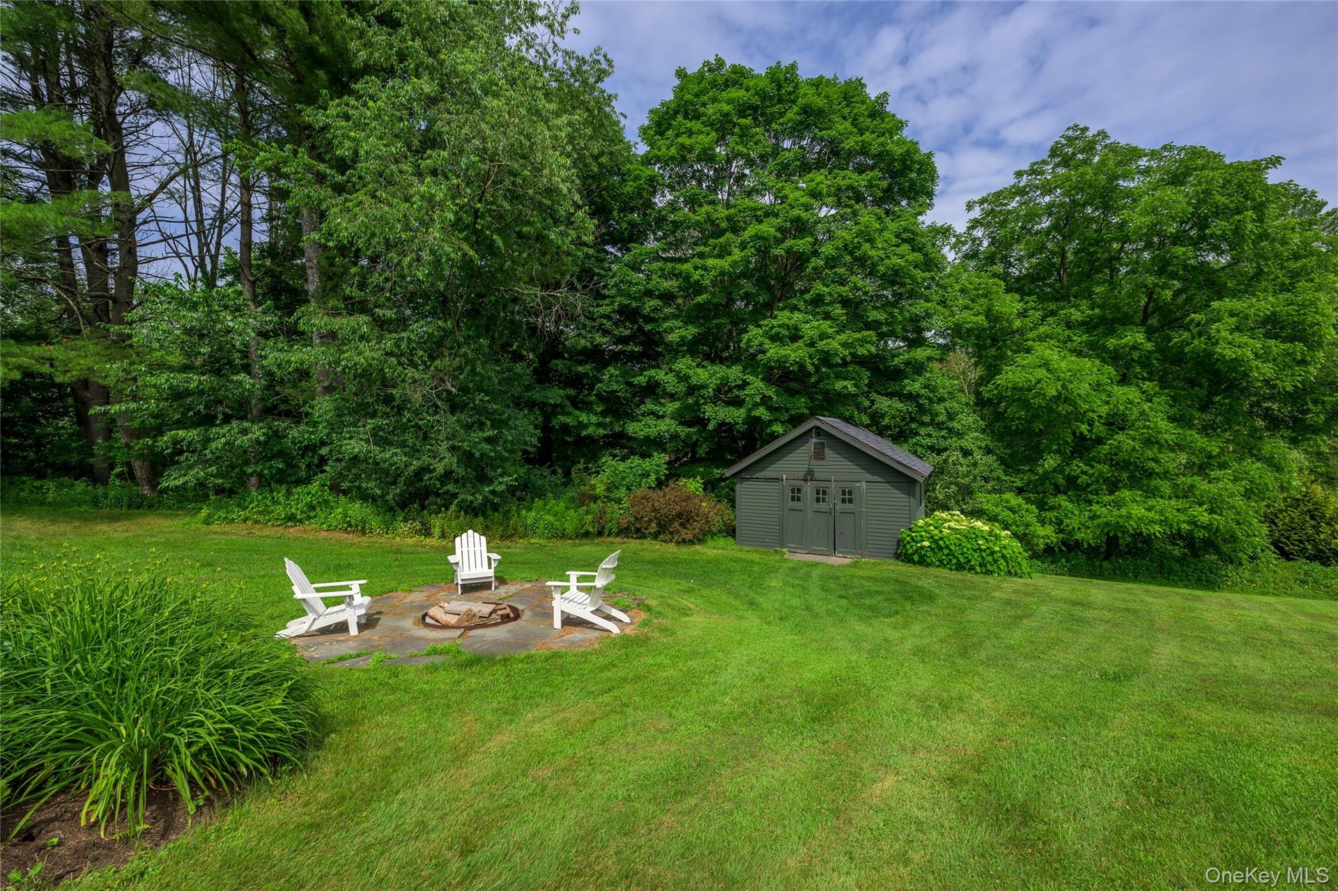 View of grassy yard featuring an outdoor fire pit, a patio, and a storage unit