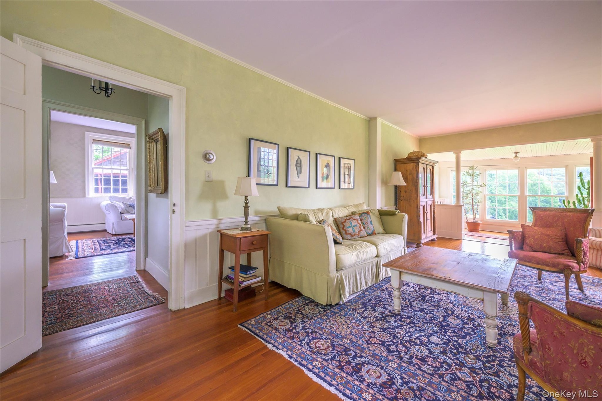 Living area with wood finished floors, plenty of natural light, a baseboard heating unit, crown molding, and wainscoting