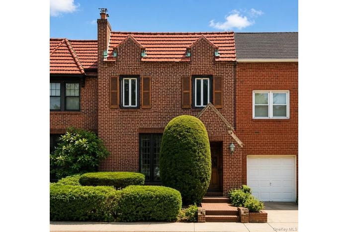 Brick facade featuring a terracotta tile roof, architectural dormers, wood shutters, and neatly sculpted shrubbery