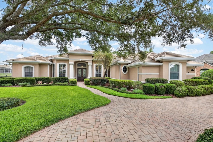 This elegant Mediterranean-inspired residence makes a striking first impression with its sweeping paver driveway, manicured landscaping, and stately a