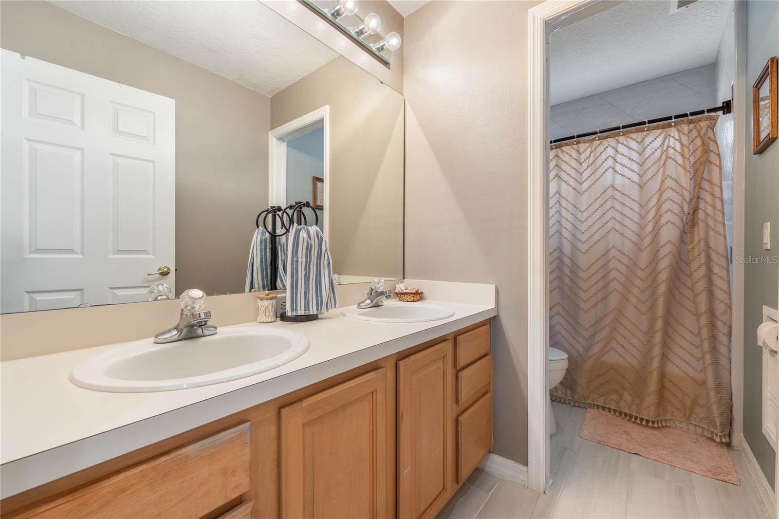 Upstairs full bathroom featuring a separated vanity area and shower, ideal for shared use and added privacy.