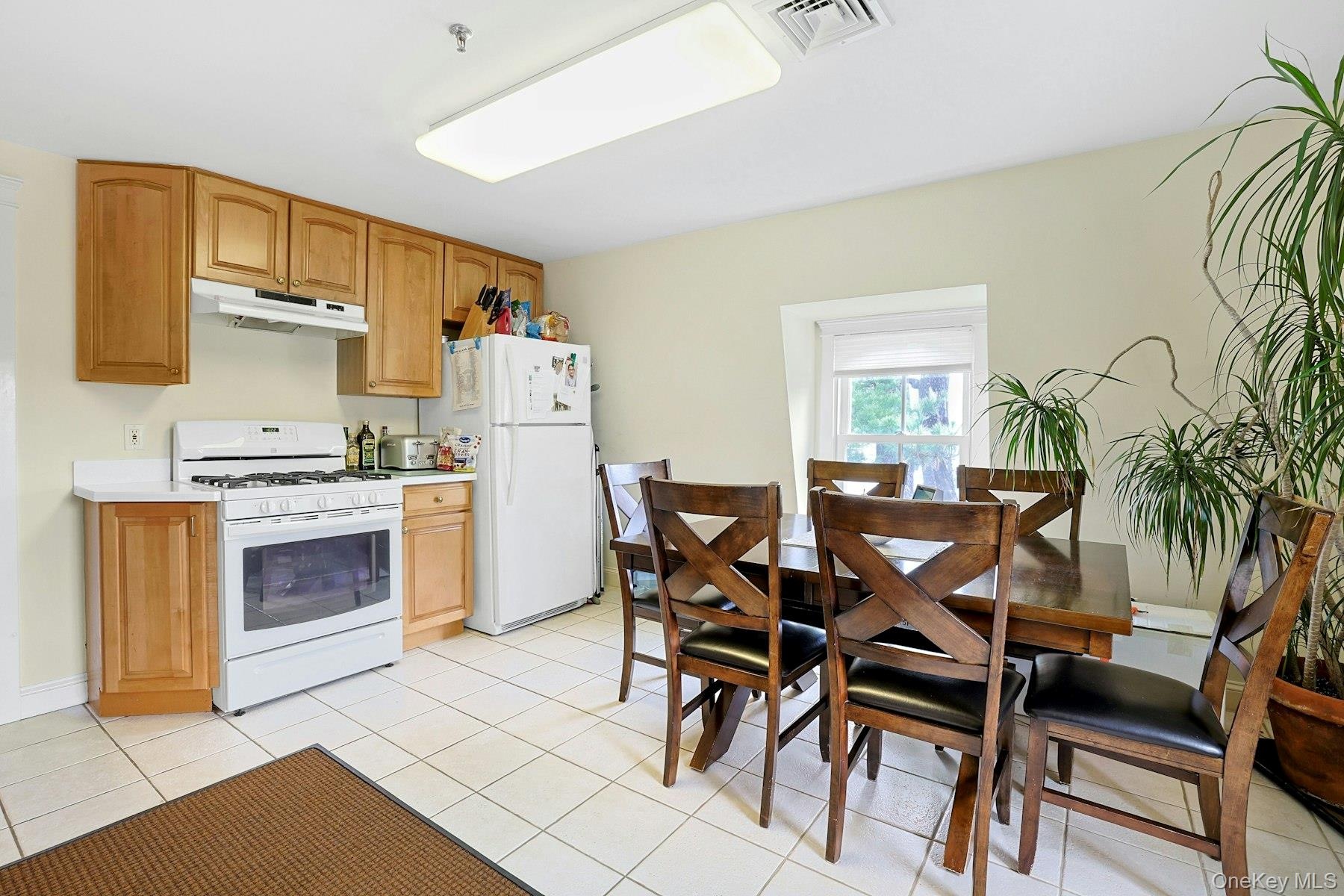 Kitchen with white appliances, light countertops, light tile patterned flooring, and under cabinet range hood
