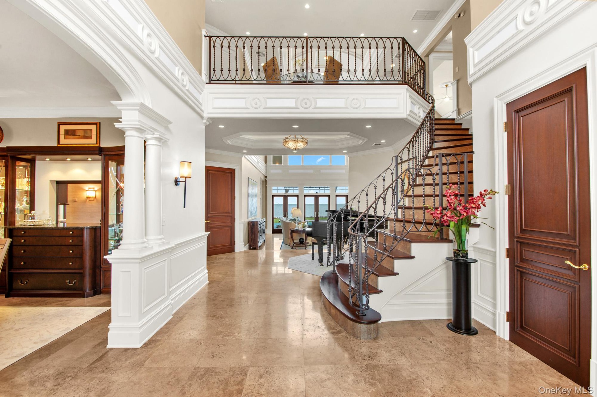 Bright 2 story entry foyer with a decorative wall, stairs, a high ceiling, crown molding, and ornate columns