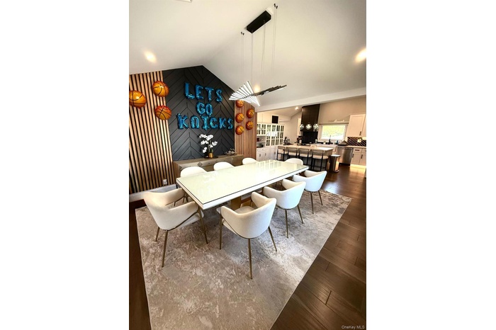 Open-concept dining area featuring dark wood-finish flooring, a modern linear chandelier, and a vaulted ceiling