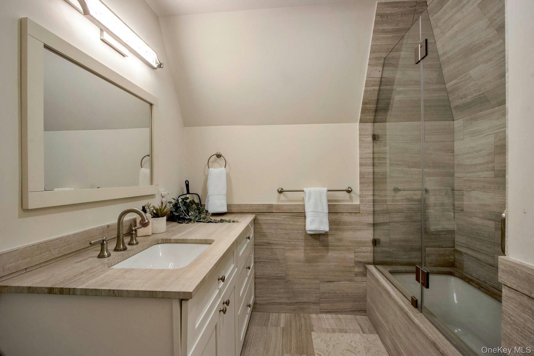 Bathroom with vanity, shower / bath combination with glass door, and vaulted ceiling