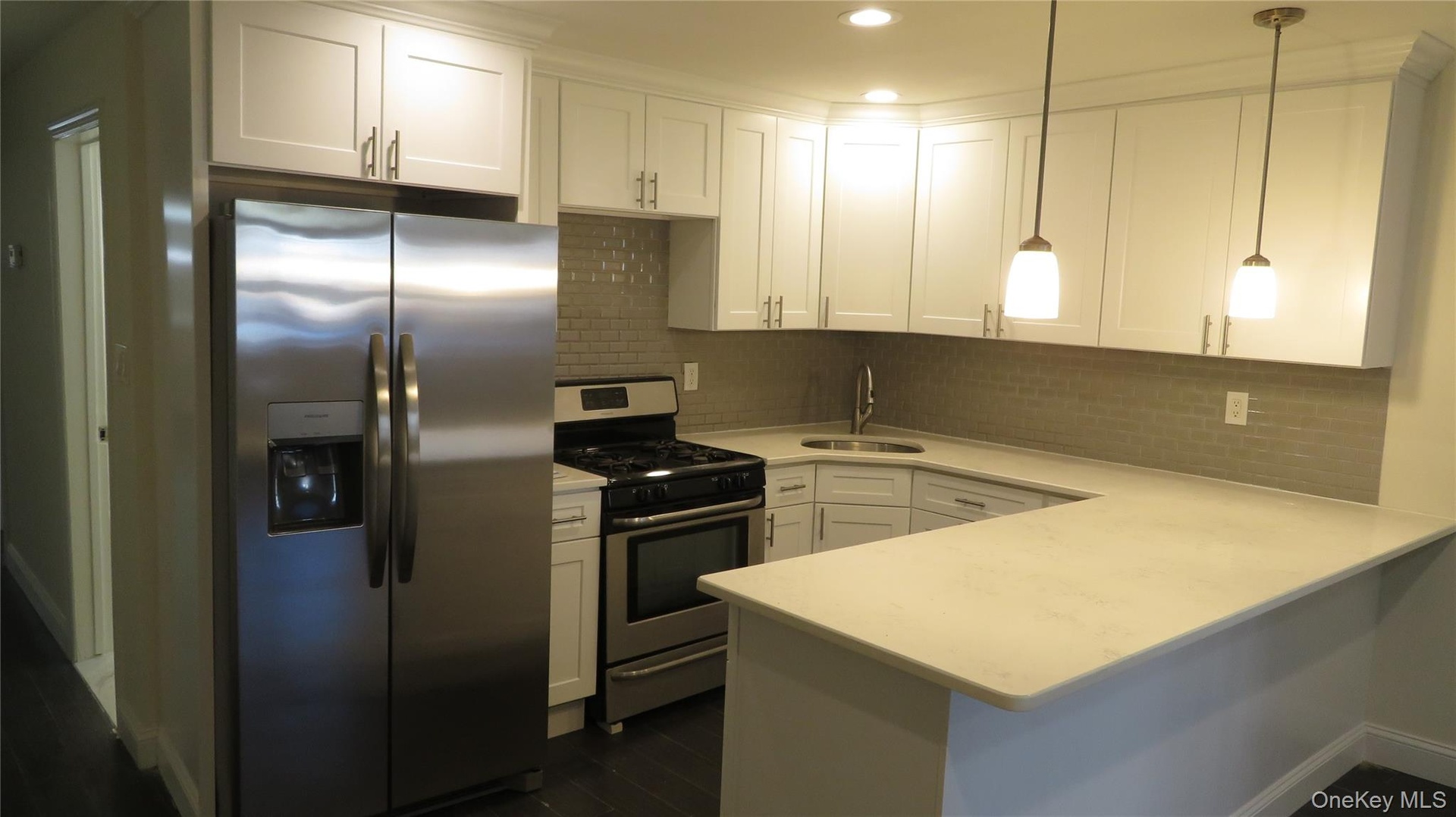 Contemporary kitchen featuring stainless steel appliances, white shaker cabinetry, a light-toned countertop, a subway tile backsplash, and dark wood-f