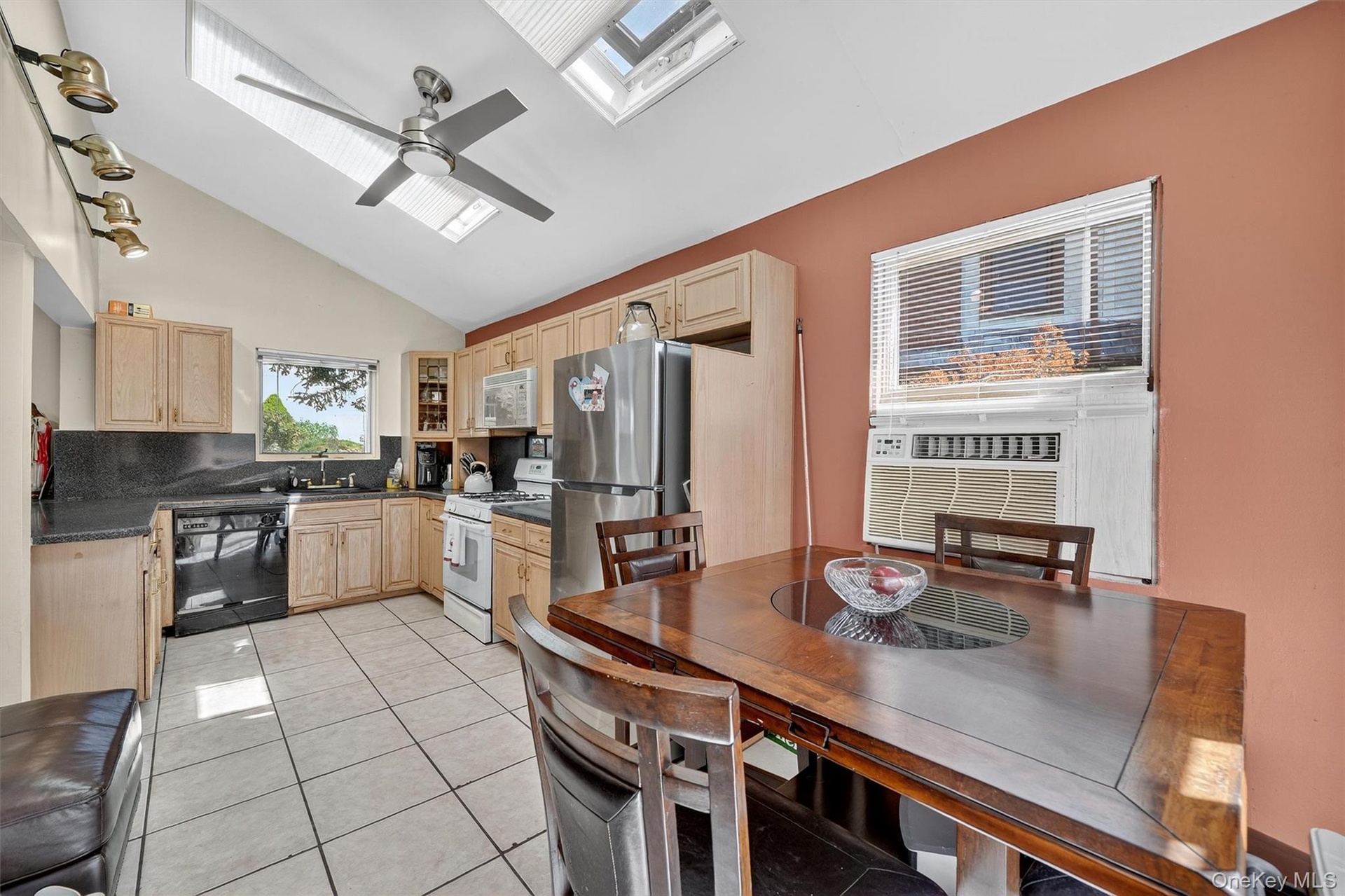 Kitchen with light brown cabinets, a skylight, light tile patterned floors, white appliances, and high vaulted ceiling