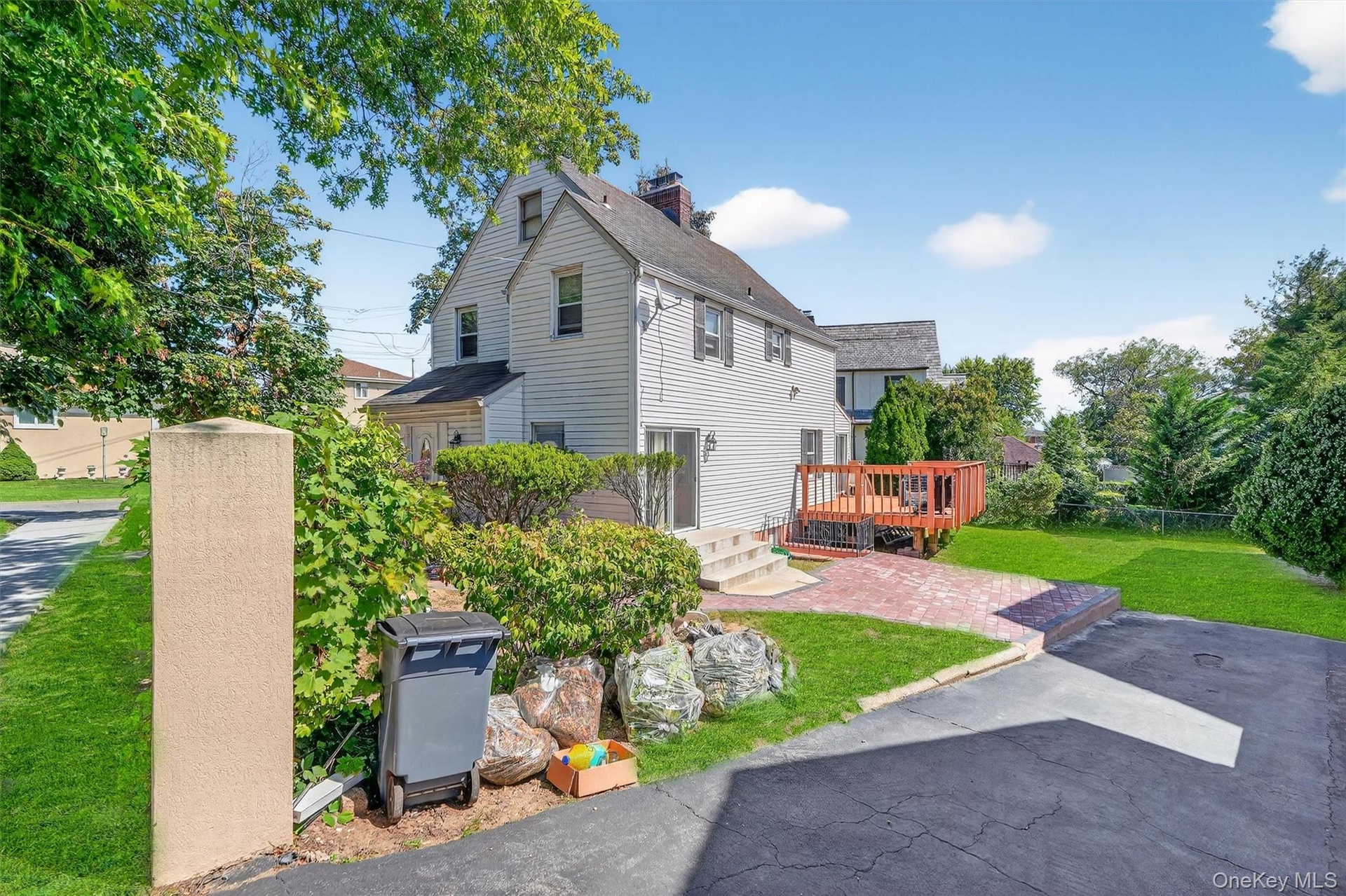 View of side of property featuring a wooden deck, a chimney, a patio, and a shingled roof