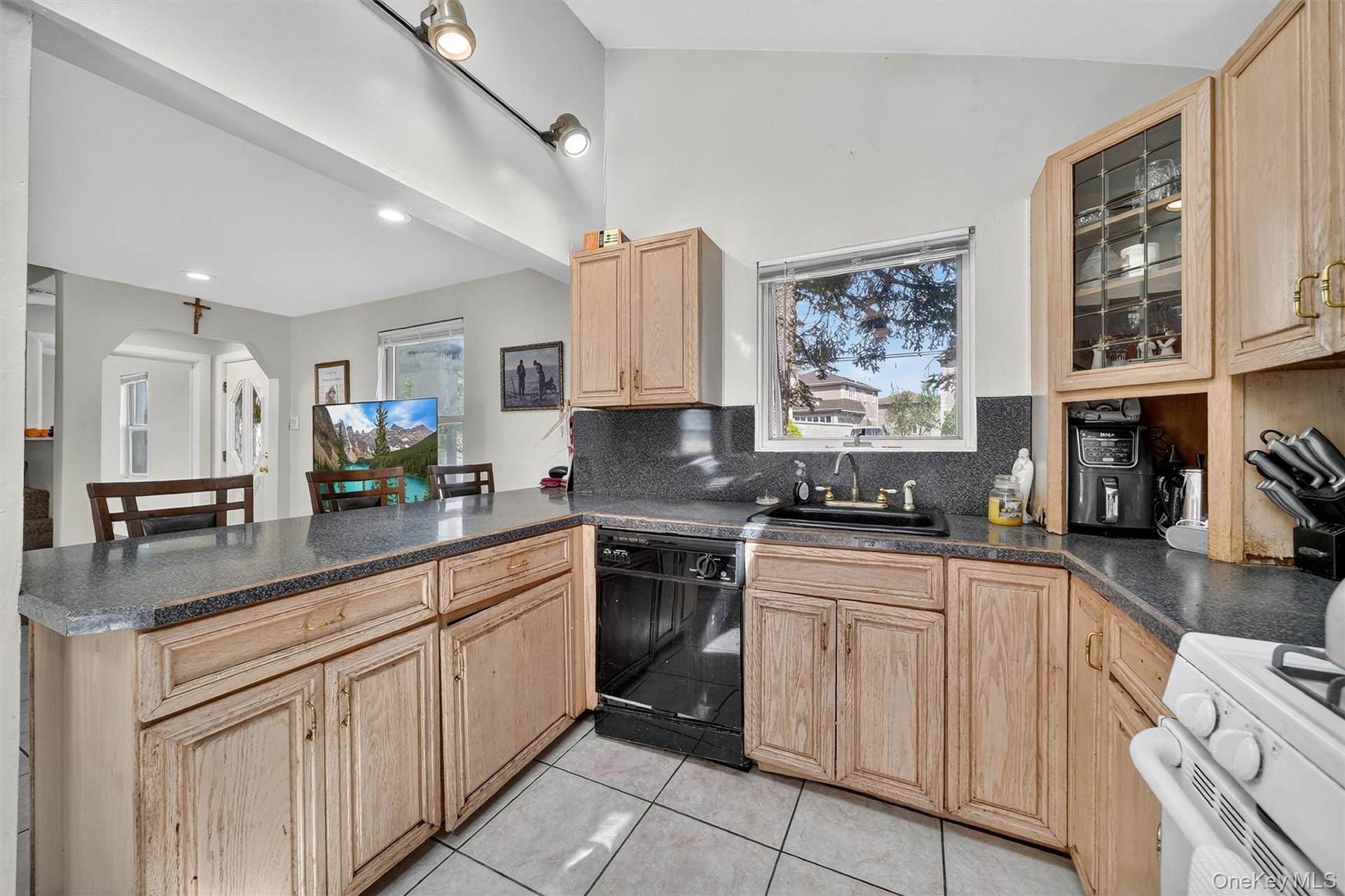 Kitchen featuring dark countertops, light brown cabinets, white range oven, a peninsula, and black dishwasher