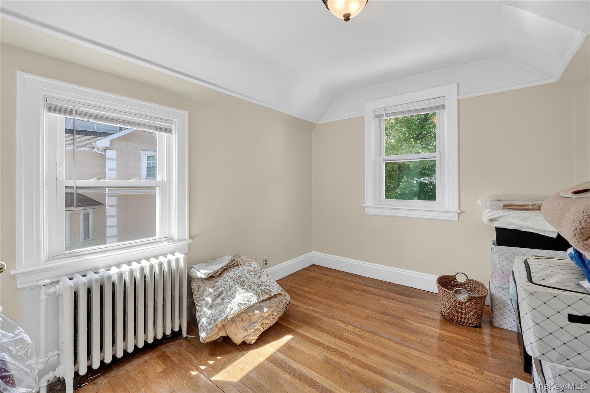 Bedroom with radiator heating unit, light wood-style flooring, and lofted ceiling