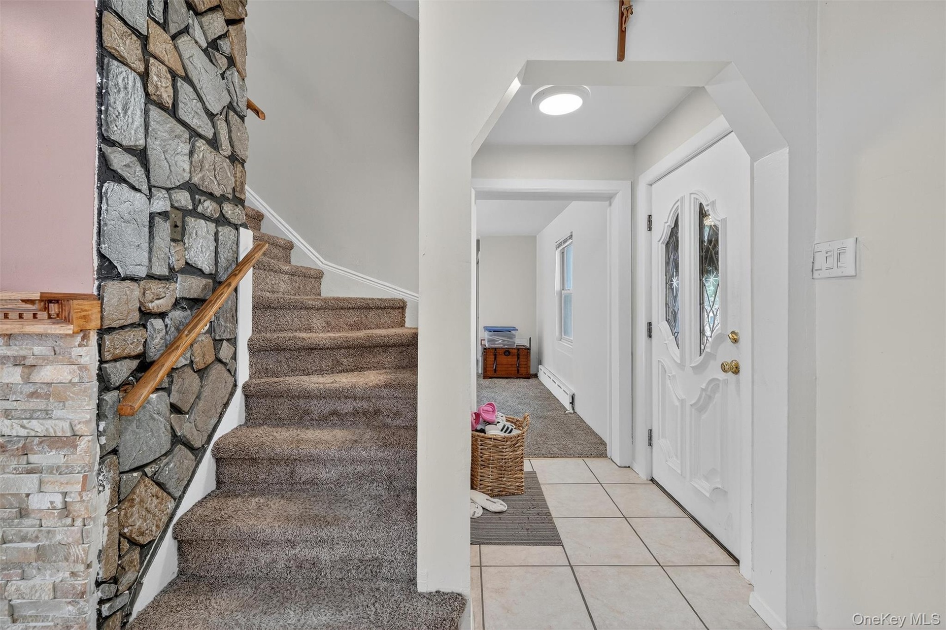 Foyer entrance featuring light tile patterned floors, light colored carpet, a baseboard heating unit, stairs, and arched walkways