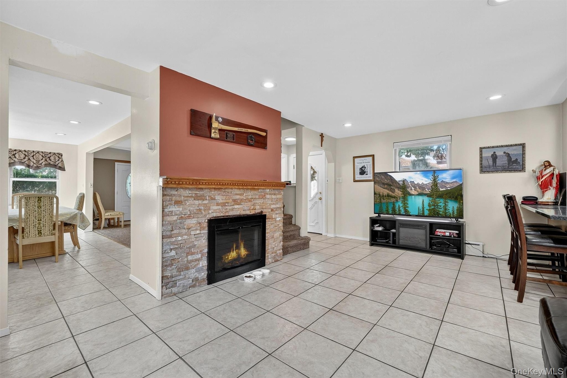 Living room featuring light tile patterned flooring, a glass covered fireplace, recessed lighting, and a baseboard heating unit