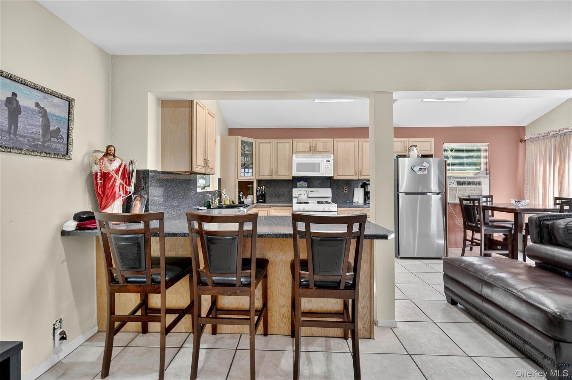 Kitchen featuring tasteful backsplash, light brown cabinets, white appliances, a kitchen bar, and dark countertops