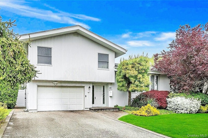 Split-level residence featuring white siding, a two-car garage, and a paver stone front walk