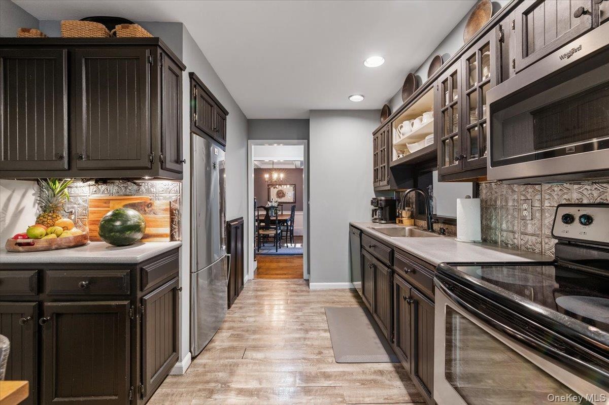 Galley kitchen featuring dark wood cabinetry, stainless steel appliances, light countertops, and wood-finish flooring