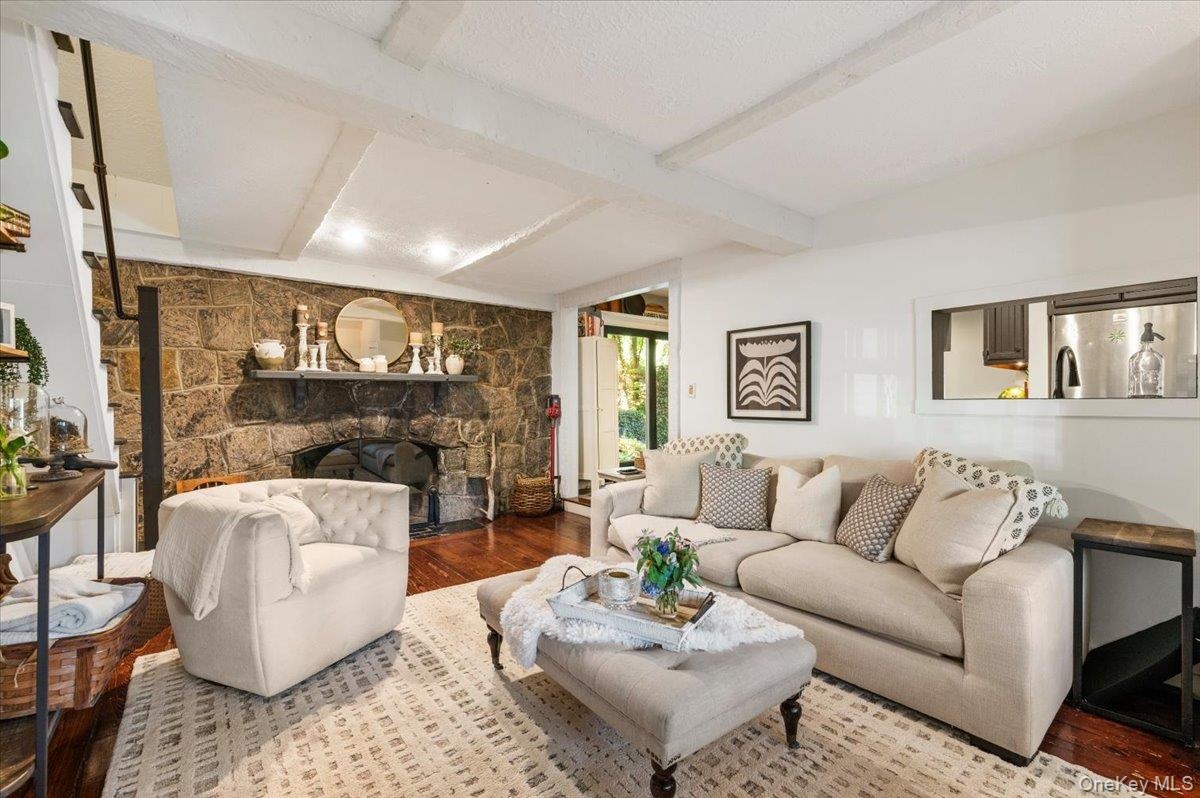 Spacious living area featuring a stone fireplace, wood-finish flooring, exposed ceiling beams, and a pass-through window