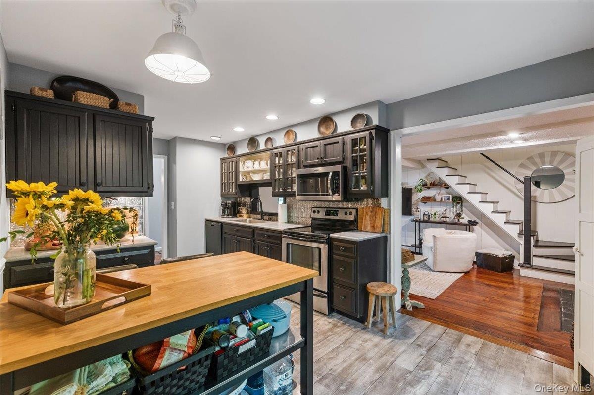Kitchen featuring dark cabinetry, stainless steel appliances, and a light wood-finish island with open shelving