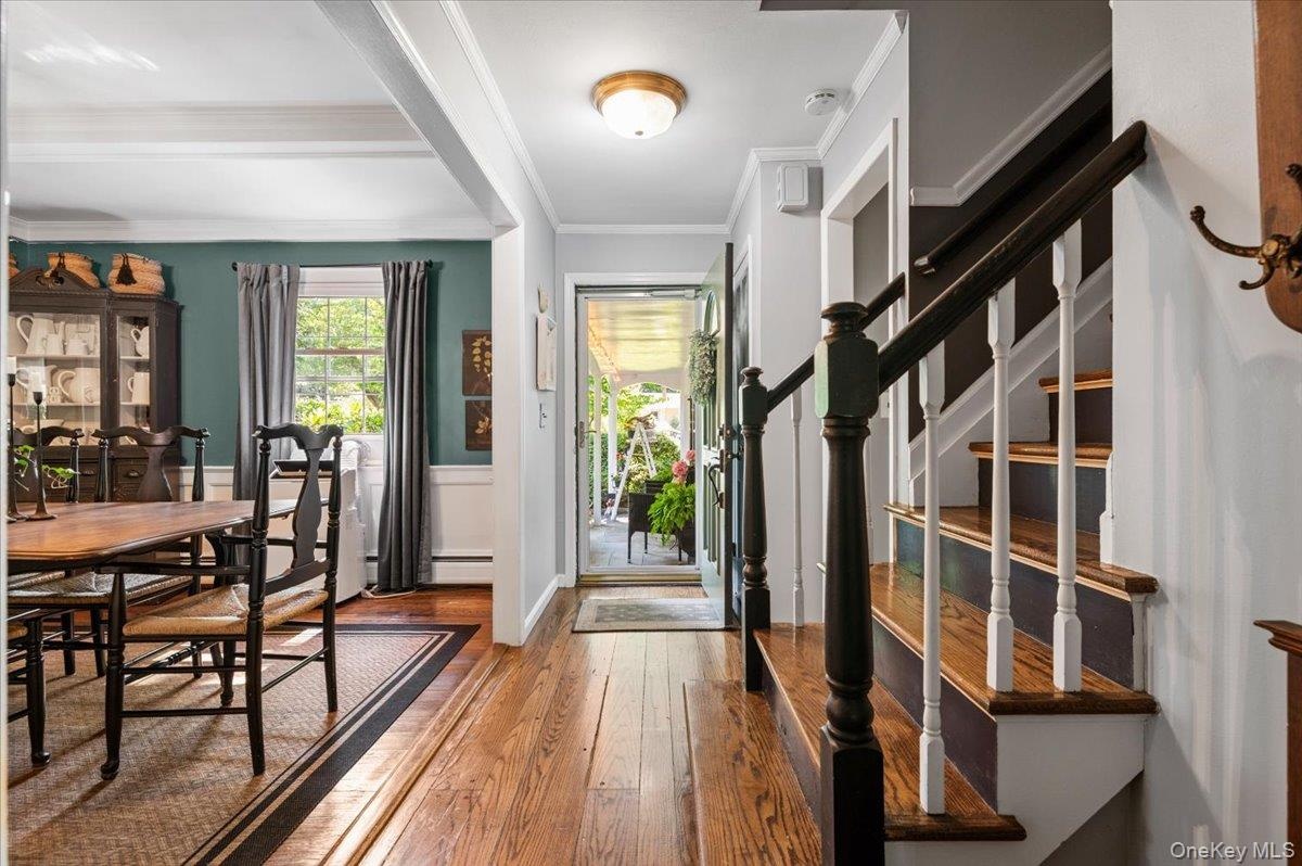 Hardwood flooring throughout entryway and dining area, featuring a staircase with contrasting dark wood handrails and white balusters, and a dining sp