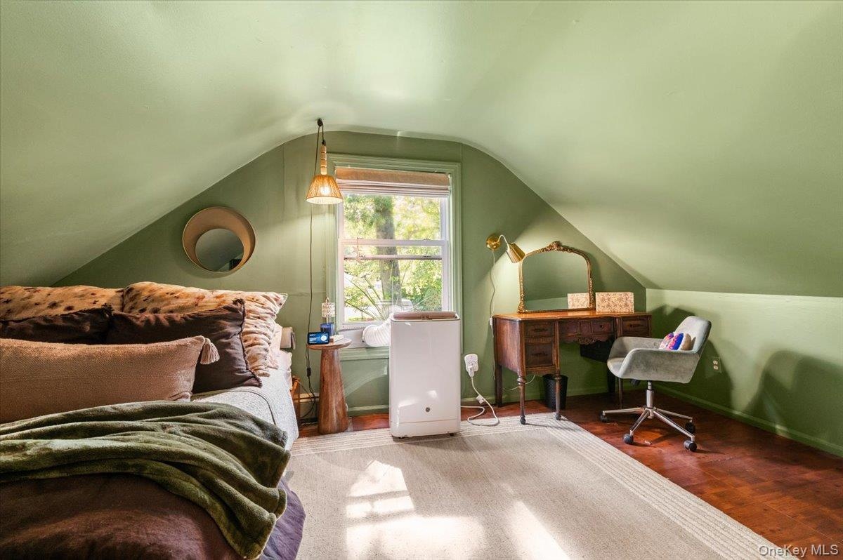 Attic space featuring sloped ceilings, hardwood flooring, and a double-pane window
