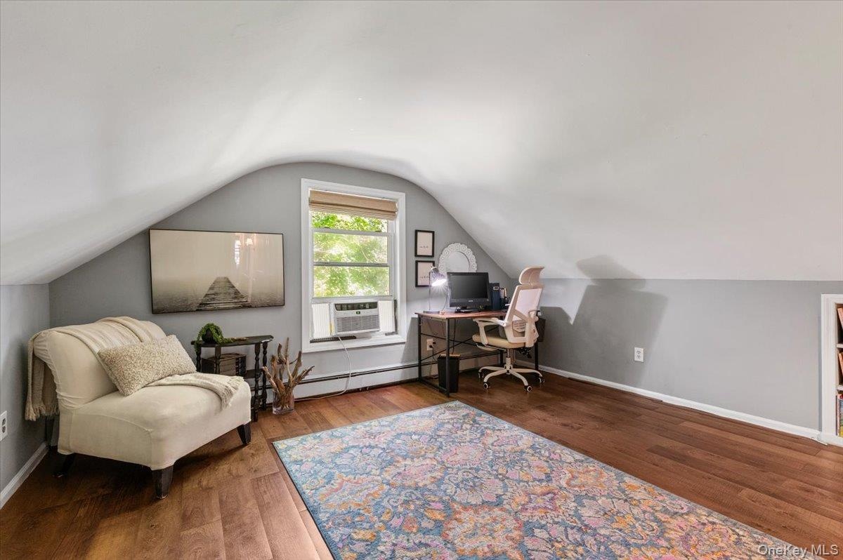 Attic living space featuring wood-finish flooring and a window with blinds