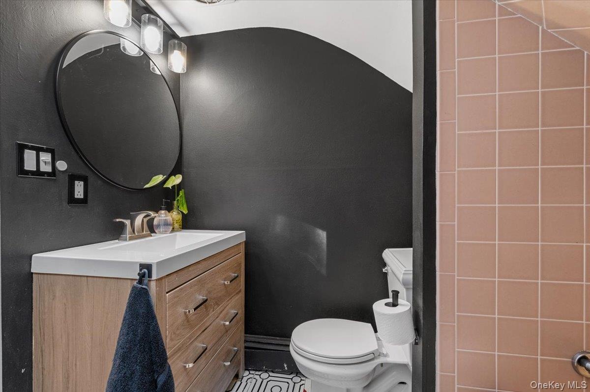 Modern bathroom featuring a wood-finish vanity with an integrated sink, brushed nickel faucet, and a circular mirror