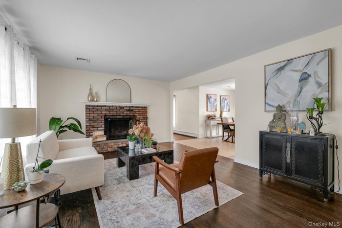 Living space with dark wood-finish flooring, a brick fireplace, and a large window