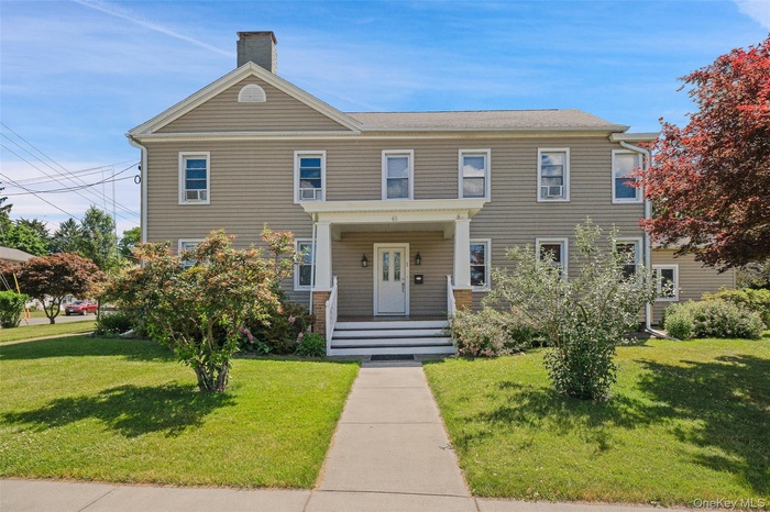 Welcoming front view of the property featuring the main entrance to Unit 1, a covered front porch with stately columns, and a landscaped front yard.