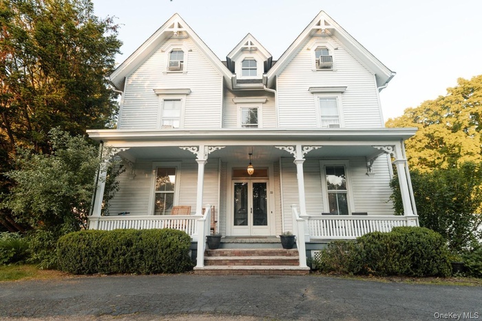 Classic white Victorian-style facade featuring multiple gables, a covered front porch with decorative brackets, a white spindle railing, and a central