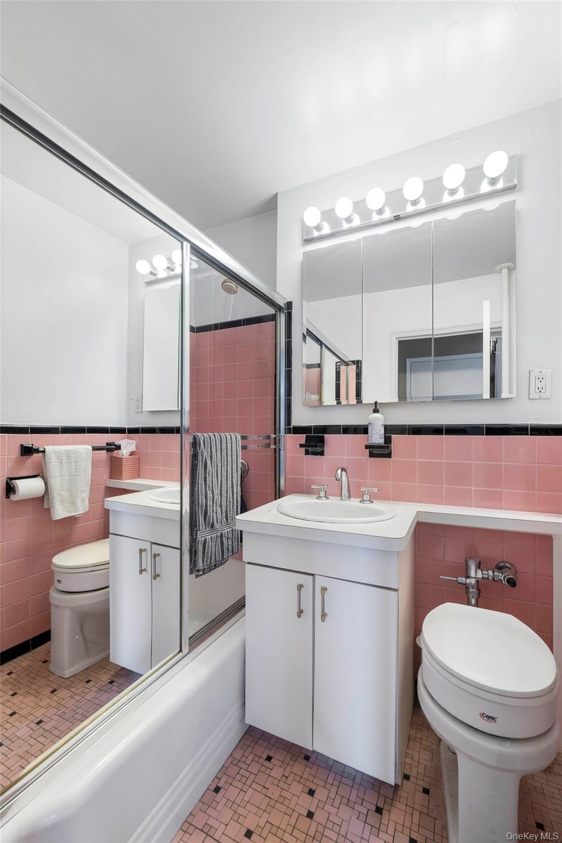 Bathroom featuring a pink and black tiled design, a white vanity with an integrated sink, a mirrored medicine cabinet, a vanity light fixture, and a s