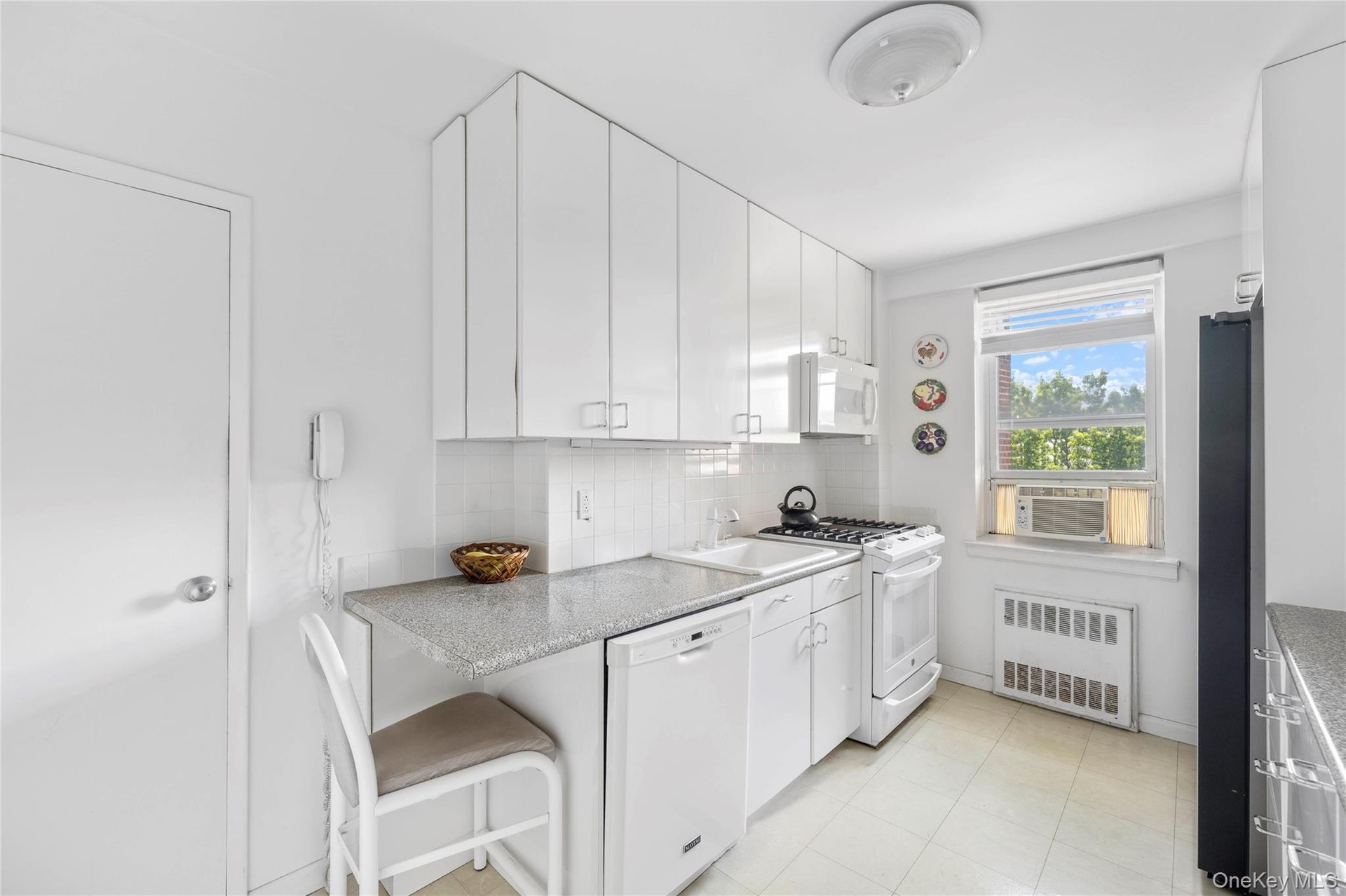 Kitchen featuring white cabinetry with silver hardware, speckled countertops, a white tile backsplash, and linoleum flooring