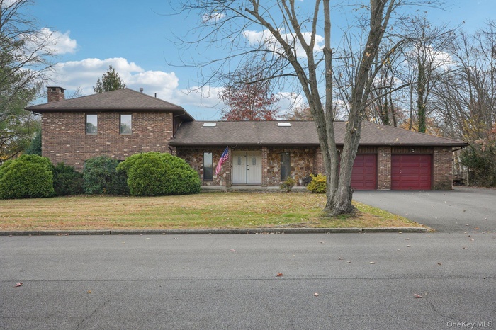 View of front of property with brick siding, asphalt driveway, a chimney, a front lawn, and an attached garage