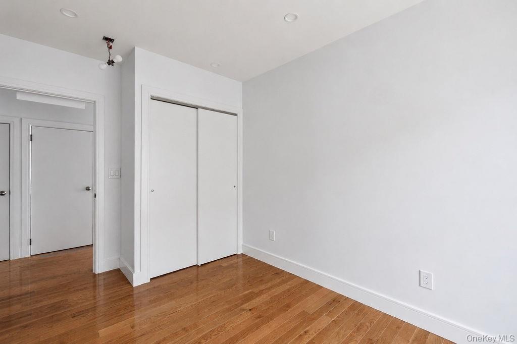 Bedroom featuring wood-finish flooring, white walls, and a built-in closet with sliding doors