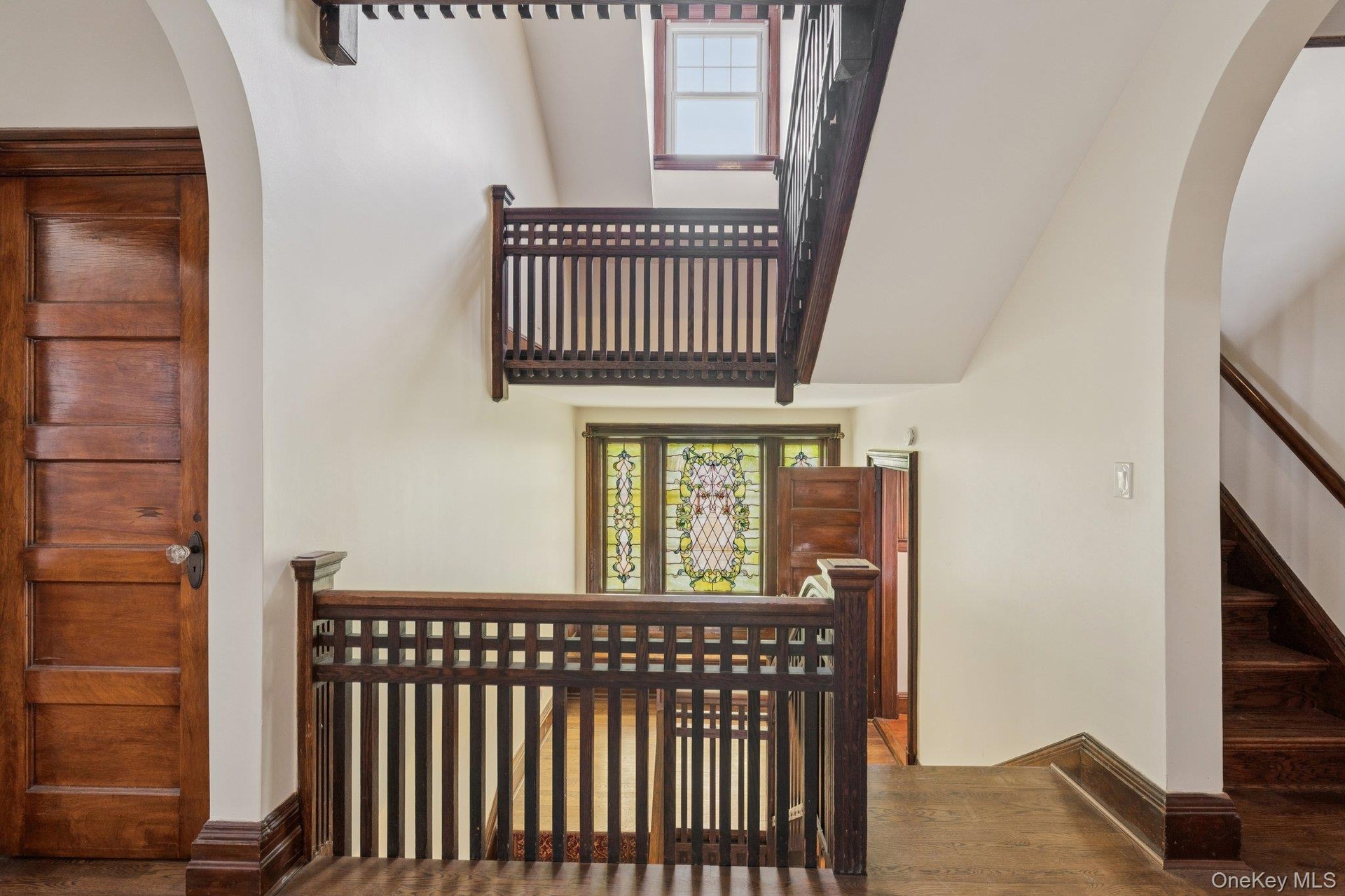 Staircase with arched walkways, plenty of natural light, wood finished floors, and a high ceiling