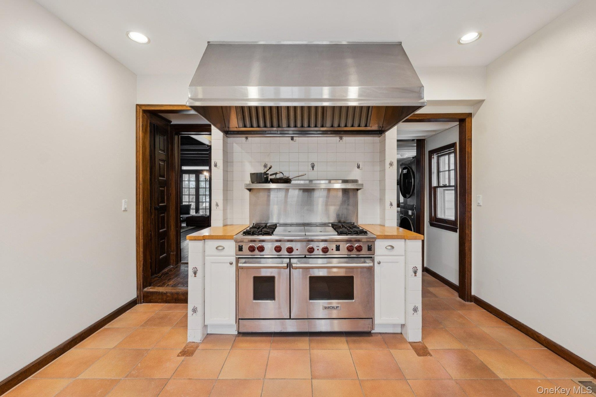 Kitchen with white cabinets, double oven range, ventilation hood, and stacked washing machine and dryer