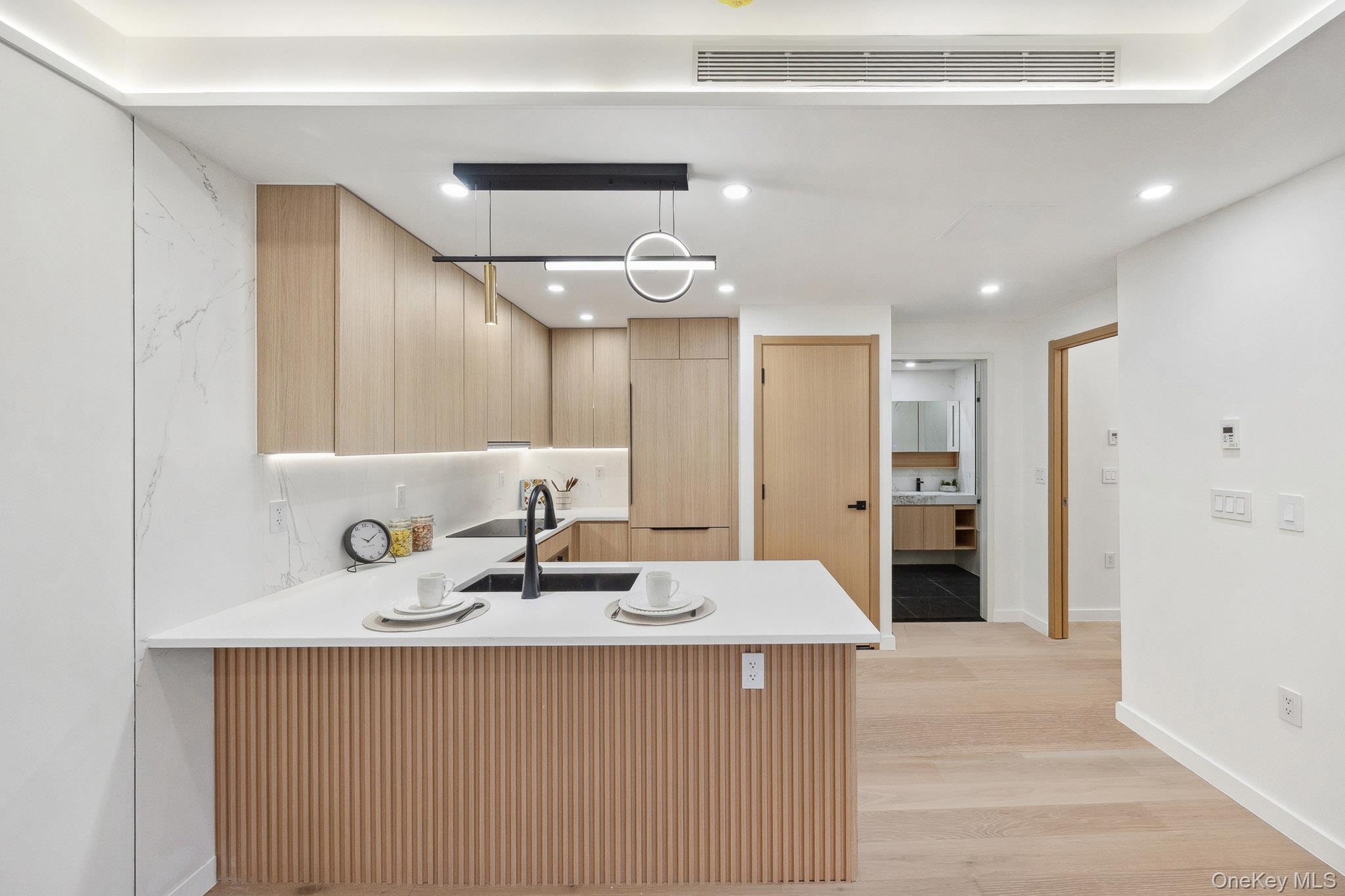 Kitchen featuring light brown cabinets, a peninsula, a sink, light wood-type flooring, and light countertops