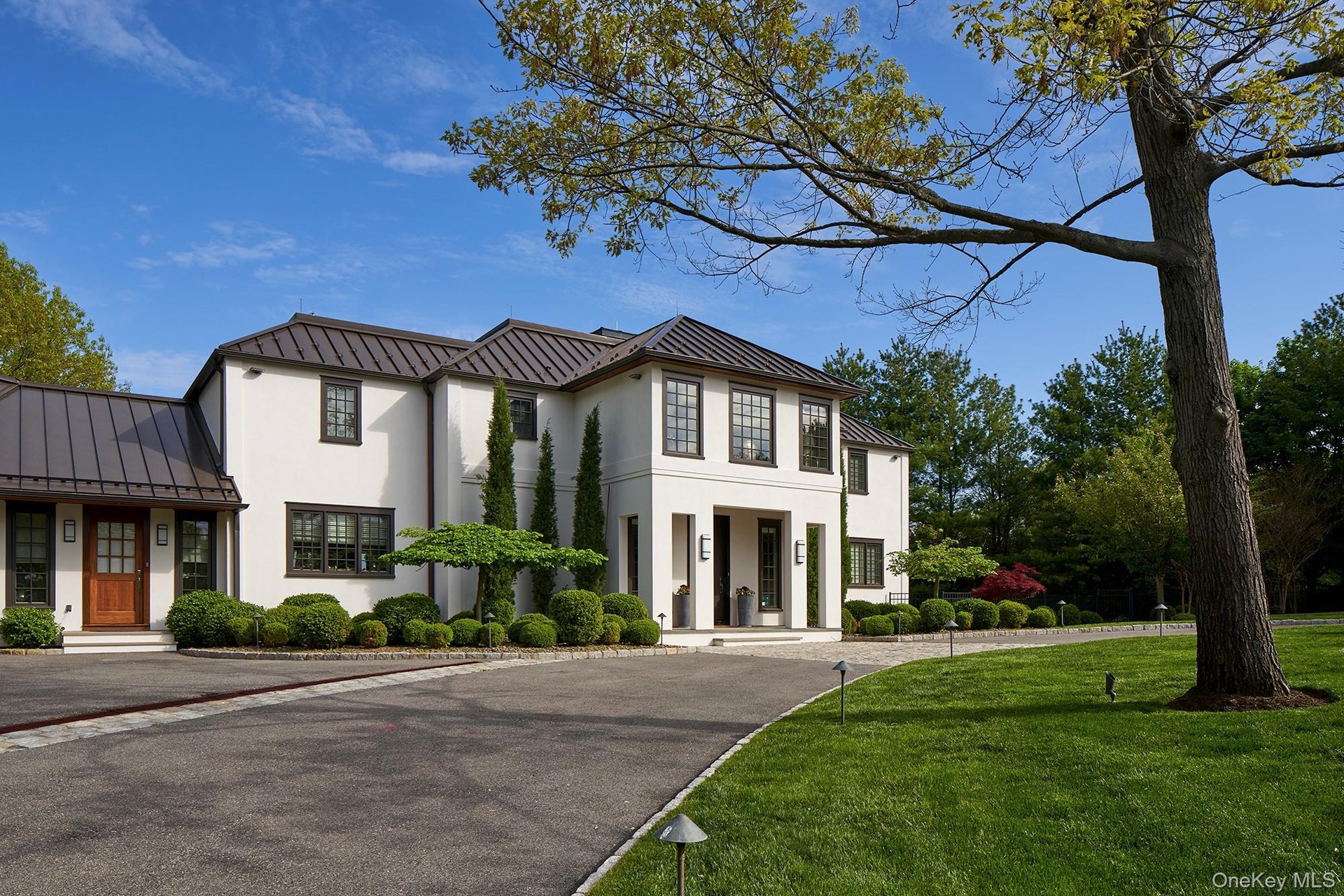 View of front of house with stucco facade, standing seam roof and circular driveway.