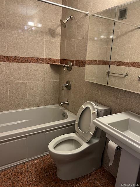 Bathroom featuring tiled shower / bath combo, toilet, and tile walls
