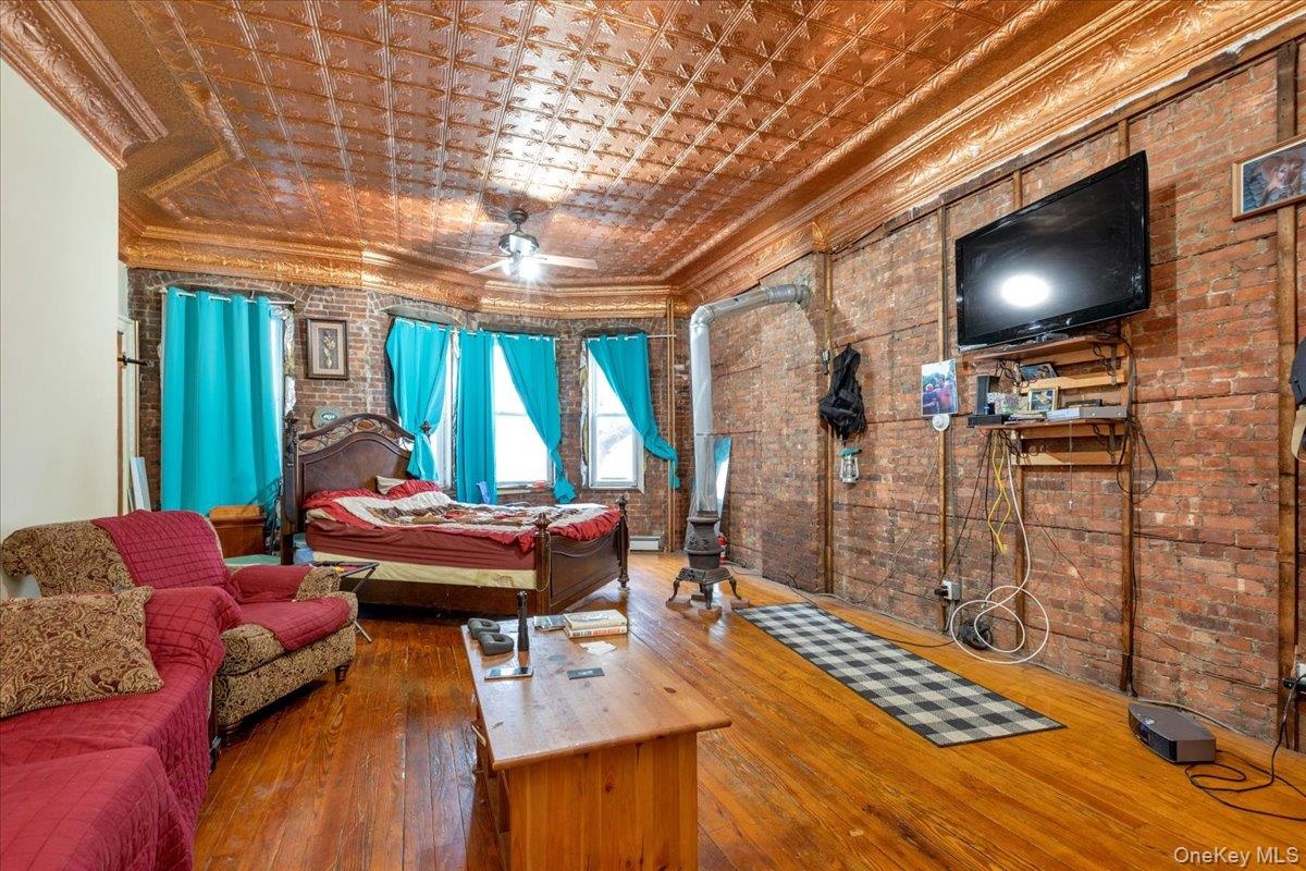 Bedroom with hardwood / wood-style flooring, a baseboard heating unit, brick wall, and ornamental molding