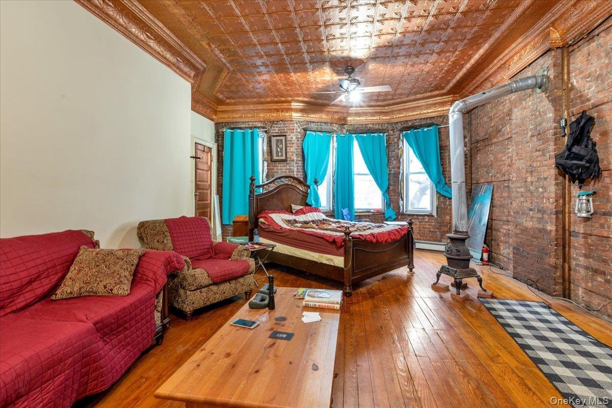 Bedroom with a baseboard heating unit, ornamental molding, hardwood / wood-style floors, and brick wall