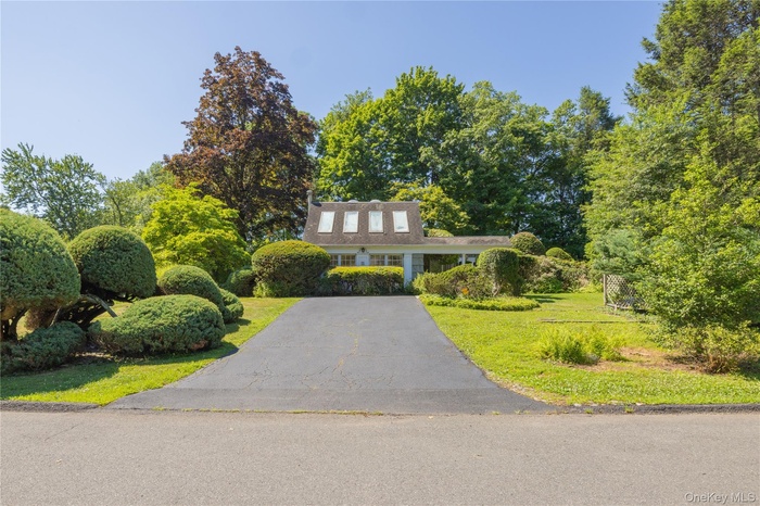 Front exterior with a paved driveway, manicured lawn, and mature trees
