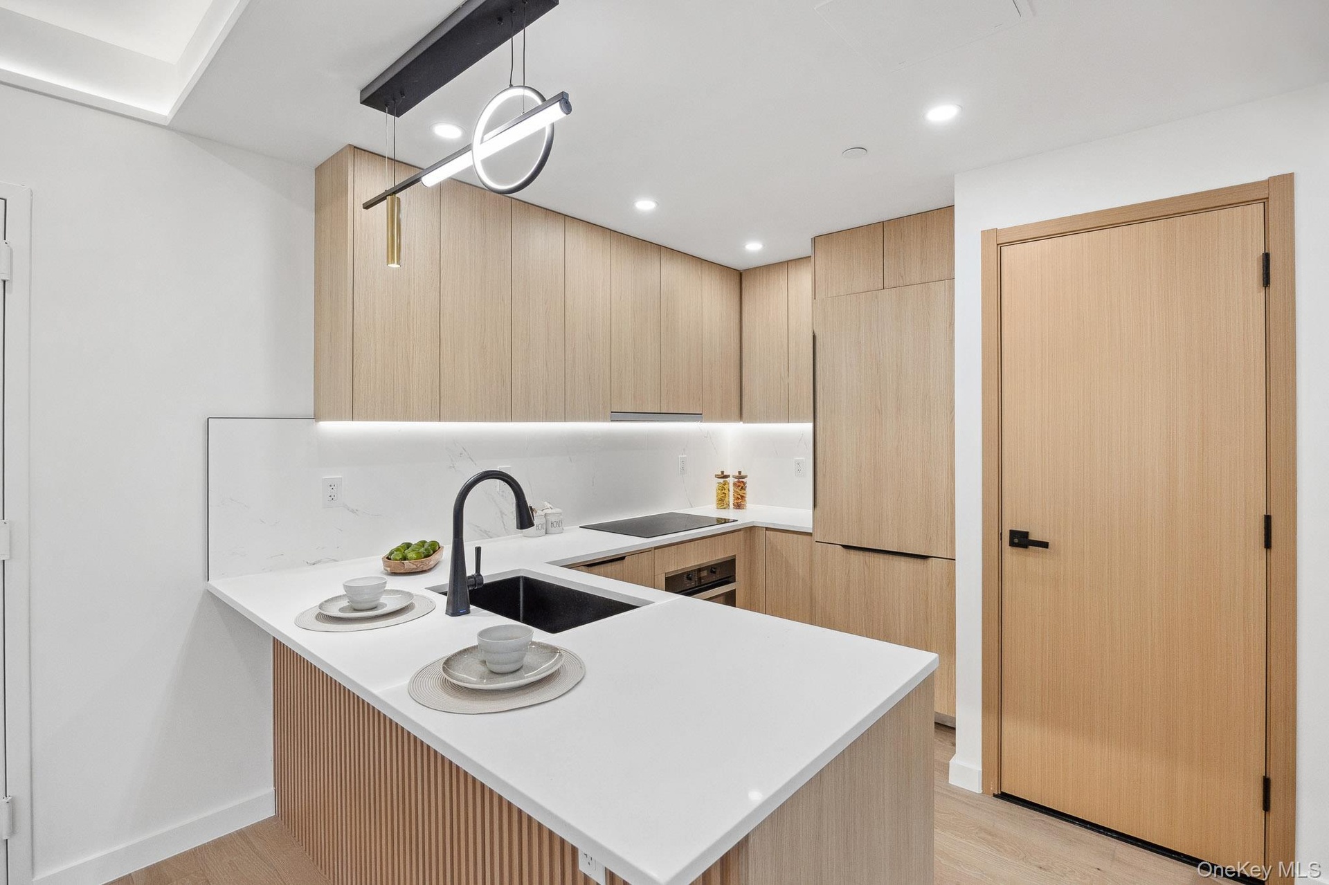 Kitchen with light brown cabinetry, a sink, light countertops, a peninsula, and light wood-style flooring