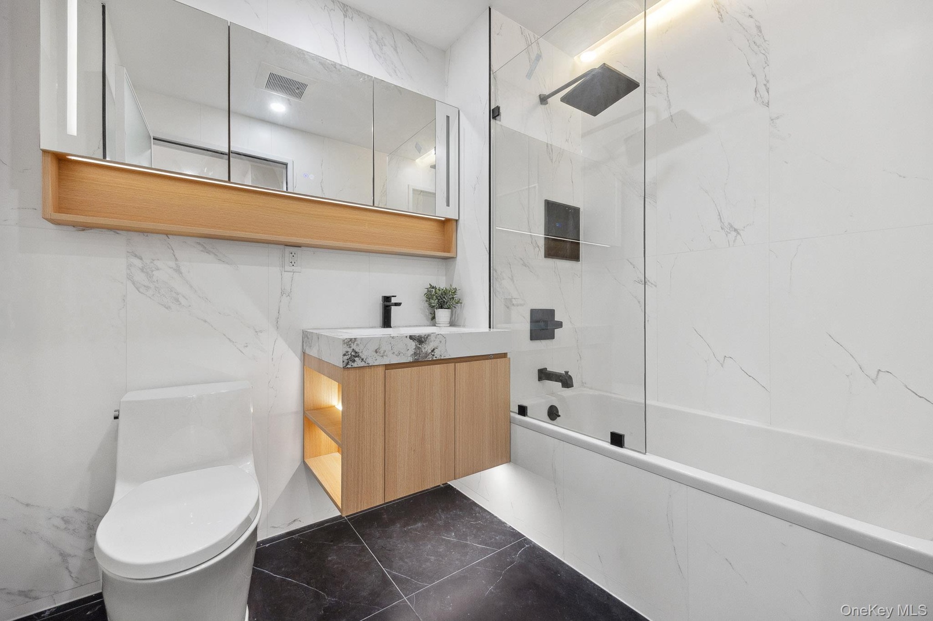 Bathroom featuring marble tiled flooring, toilet, a combined bath / shower with marble appearance, and vanity