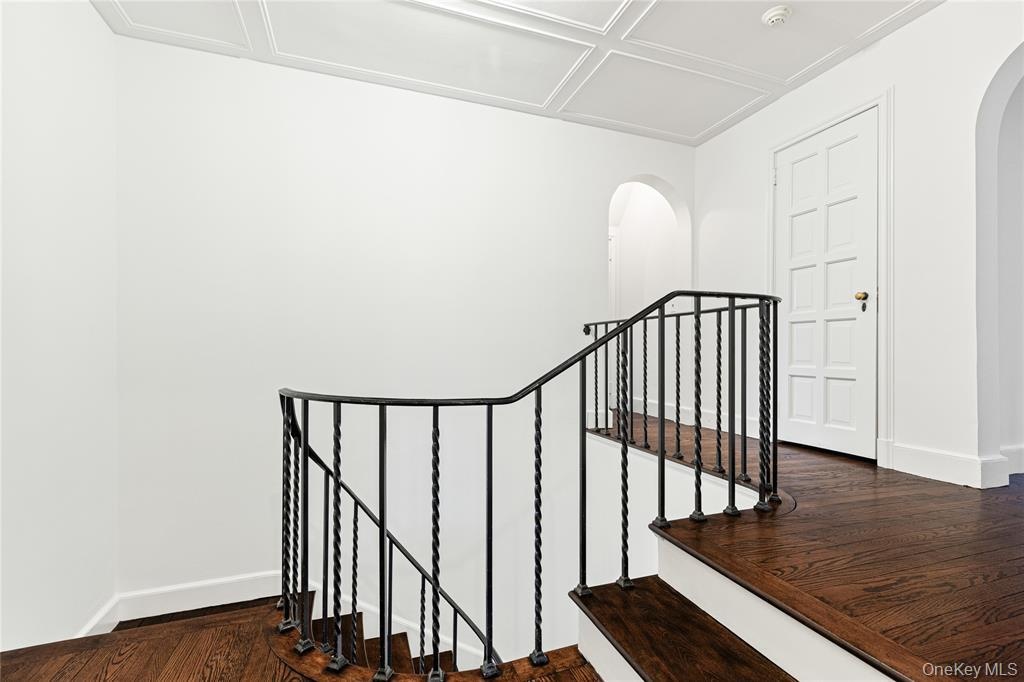 Stairs with arched walkways, wood finished floors, and baseboards