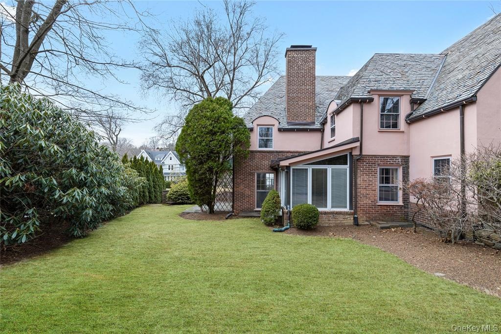 Back of property featuring a lawn, a chimney, brick siding, and stucco siding