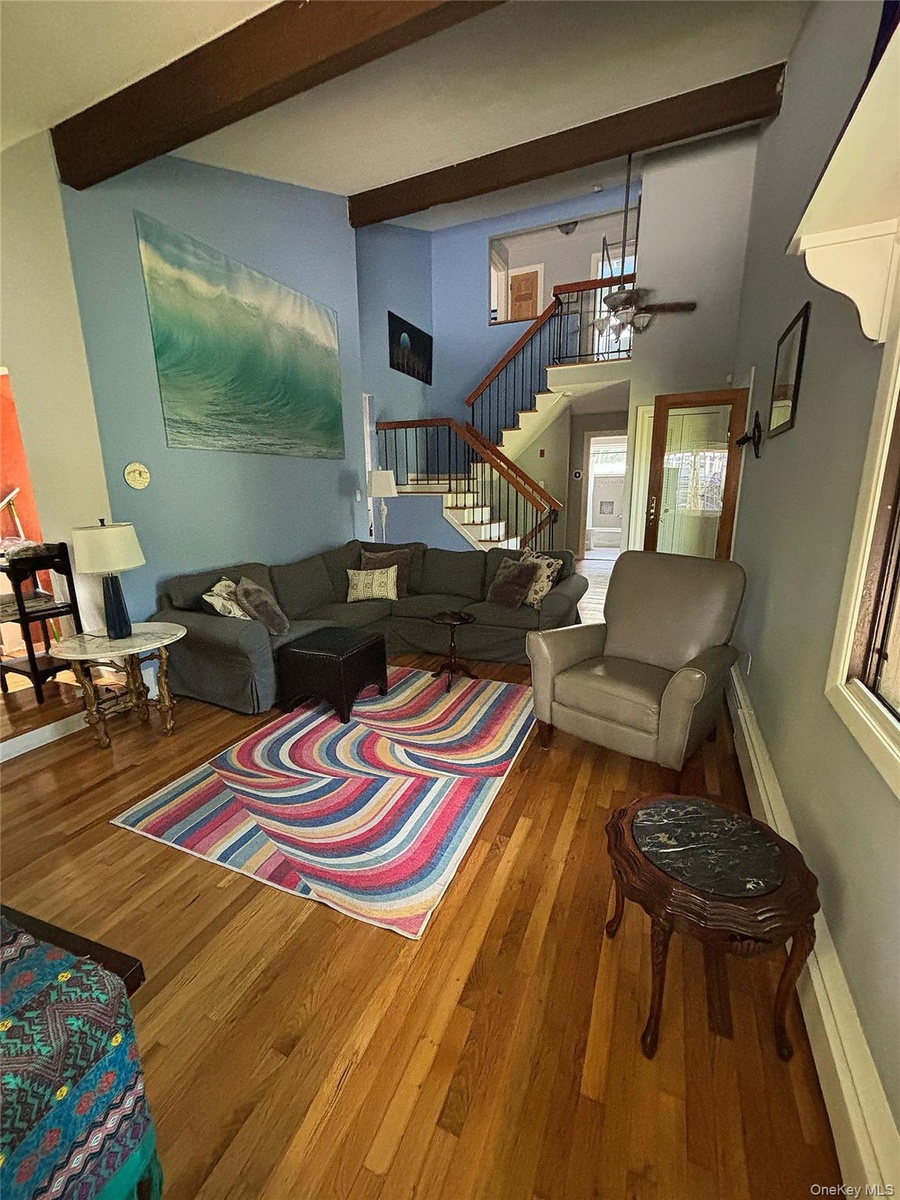 Front Living area featuring high ceilings with exposed wood beams, hardwood flooring, and a multi-level staircase with wood handrails and black metal 
