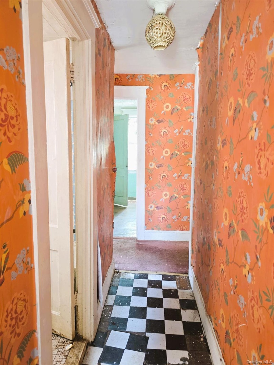 Hallway featuring checkerboard tile flooring, ornate flush-mount ceiling light fixture, and patterned wallpaper