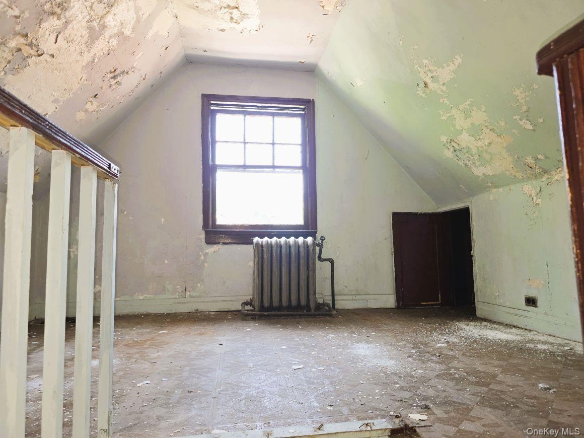 Attic- front room  space featuring an operable window with wood trim, a vintage-style radiator, and a built-in storage door